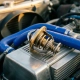 Precision automotive thermostat with open metallic housing showing internal mechanisms on engine bay surface with cooling pipes