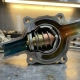Cutaway automotive thermostat housing showing wax element expansion with thermal stress patterns on metallic components and coolant passages displaying temperature gradients