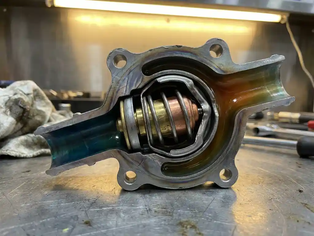 Cutaway automotive thermostat housing showing wax element expansion with thermal stress patterns on metallic components and coolant passages displaying temperature gradients