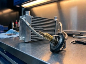 Automotive thermostat with exposed wax sensing element beside transmission cooling system on workshop bench under bright lighting