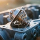 Chrome automotive thermostat with valve mechanisms on frost-covered engine block, morning condensation droplets in golden sunrise light