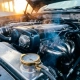 Car engine bay at dawn with frost-covered surfaces, vapor rising from exhaust, and precision thermostat component in foreground