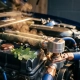 Modern car engine bay with precision thermostat in foreground, golden steam rising from coolant lines, green leaf on engine block