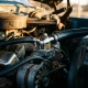 Chrome thermostat housing with coolant hoses in weathered truck engine bay under golden hour lighting