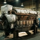 Massive diesel engine block with exposed copper cooling channels and orange heat signatures in industrial workshop