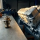 Precision thermostat component beside car engine block with melting frost crystals in golden morning sunlight