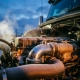 Commercial truck engine bay at dawn with chrome thermostat housing in foreground, frost crystals on metal surfaces catching golden sunrise light