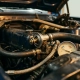Automotive thermostat component inside open engine bay, surrounded by coolant hoses and metal tubing with temperature gauge visible nearby.
