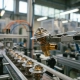 Robotic arm assembling a brass thermostat valve on an automotive manufacturing conveyor line with stainless steel parts in soft industrial lighting.