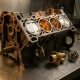 Cross-sectioned car engine block revealing pistons in cylinders, with a precision thermostat component on a steel workshop surface.