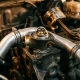 Precision-machined engine thermostat inside a disassembled car engine bay with aluminum cooling pipes and worn piston in background.