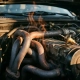 Clogged exhaust pipes under an open car hood with heat shimmer rising above corroded bends and a thermostat resting on the engine block.