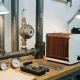 Industrial thermostat mounted on heavy steel pipes beside a residential heating unit, with calibration tools and temperature gauges on a workbench.