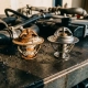 Corroded automotive thermostat valve with mineral deposits next to a new replacement part on a grease-stained workshop surface.