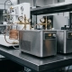 Two precision thermostats on a steel lab bench, one connected to copper tubing and temperature gauges, with condensation on metal surfaces.