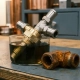 Precision thermostat with brass and stainless steel fittings half-submerged in dark industrial coolant, corroded sacrificial iron fitting alongside.
