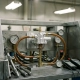 Precision thermostat component mounted in an open industrial test bench with fluid hoses, temperature gauges, and calibration instruments.
