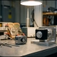 Two thermostats on a precision engineering workbench, one connected to calibration instruments with sensor probes, under focused laboratory lighting.