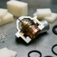 Thermostat housing split open on steel workbench, exposing brass and polymer layers beside aluminum chips and rubber seals under studio lighting.