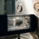Precision thermostat component undergoing water jet ingress protection testing in a stainless steel chamber with industrial gauges.