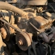 Worn serpentine belt straining around an alternator pulley in an engine bay with oil residue and heat shimmer on dark cast components.