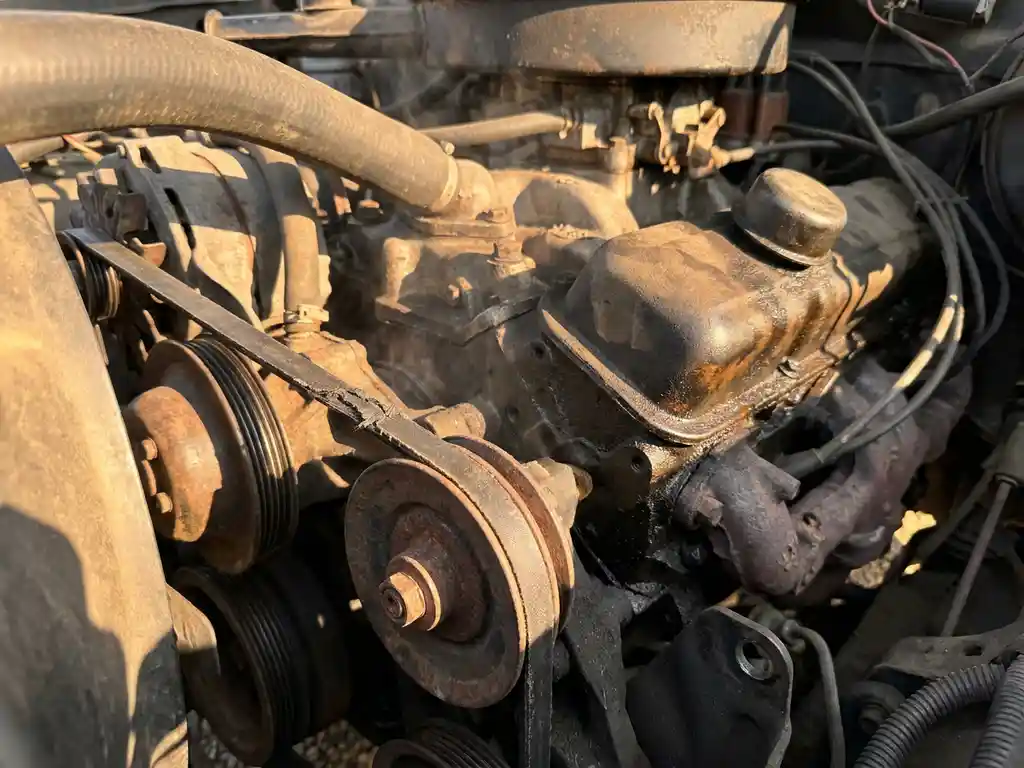 Worn serpentine belt straining around an alternator pulley in an engine bay with oil residue and heat shimmer on dark cast components.