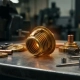 Brass thermostat bellows capsule mid-expansion on a polished steel workbench, surrounded by precision-machined components and copper fittings.