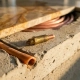 Brass wax pellet thermostat element on a cross-section of radiant floor heating pipe embedded in concrete screed beneath polished stone tile.