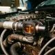 Precision thermostat housing mounted in an open engine bay, with amber coolant visible through a cutaway cross-section amid copper-toned hoses and pipes.