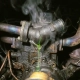 Cracked thermostat housing leaking green coolant onto a corroded engine block with steam rising and heat-stressed metal components visible.
