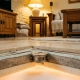 Precision thermostat embedded in a warm floor cross-section, showing layered radiant heating beneath polished stone tiles with amber glow.
