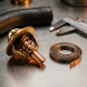 Disassembled wax pellet thermostat and bimetallic strip on stainless steel surface with engine coolant hose and calipers nearby.