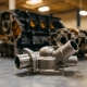 Precision-machined thermostat housing with coolant ports and mounting flanges on a metal workshop surface, engine block blurred in background.