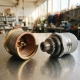 Thermostat valve and brass bellows component on stainless steel surface, macro view showing intricate coiled metal interior and mechanical detail.