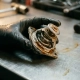 Mechanic inspecting a corroded thermostat valve with mineral deposits and coolant stains under workshop lighting.