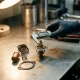 Gloved technician measuring a disassembled wax pellet thermostat valve stem with precision calipers on a steel workshop surface.
