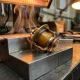 Cross-sectioned wax thermostat element revealing waxy interior on a precision machined metal surface with heat shimmer in warm workshop lighting.